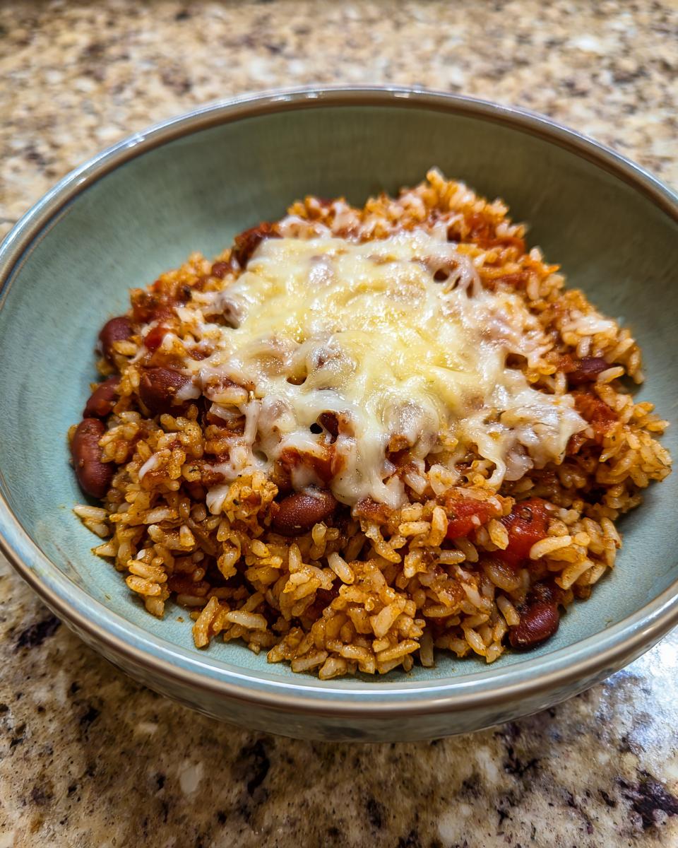 Plato de arroz con frijoles y tomate, cubierto con queso derretido, ideal para recetas económicas para familia.
