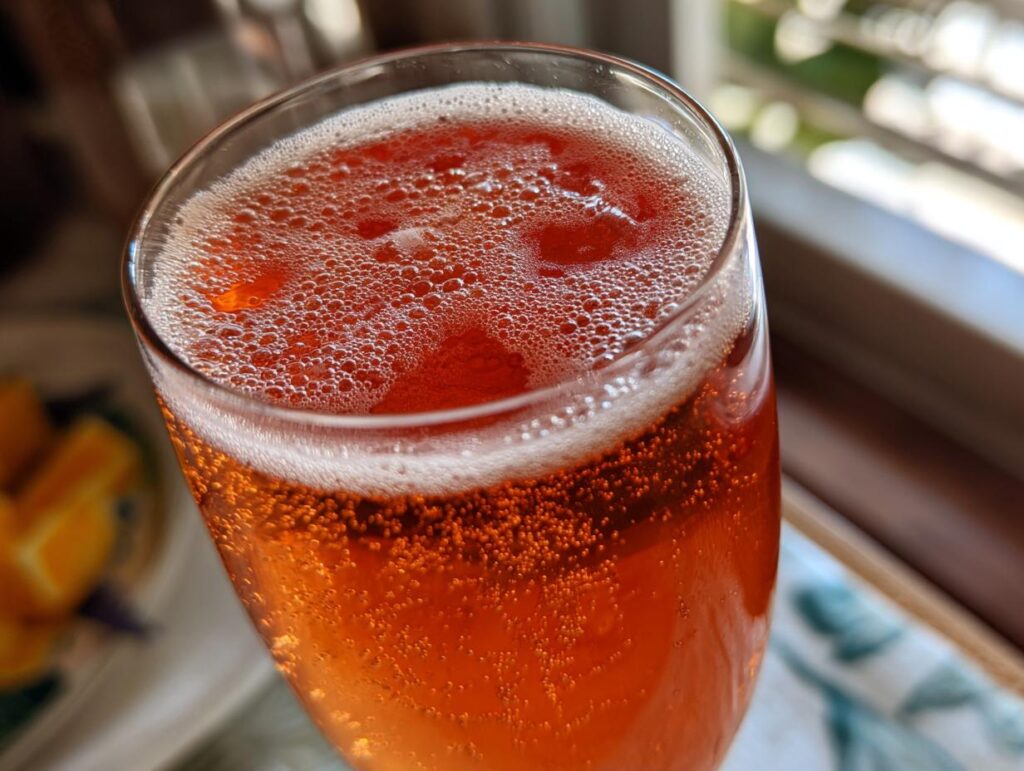 Primer plano de un vaso de cócteles de Año Nuevo de color naranja con burbujas y espuma.