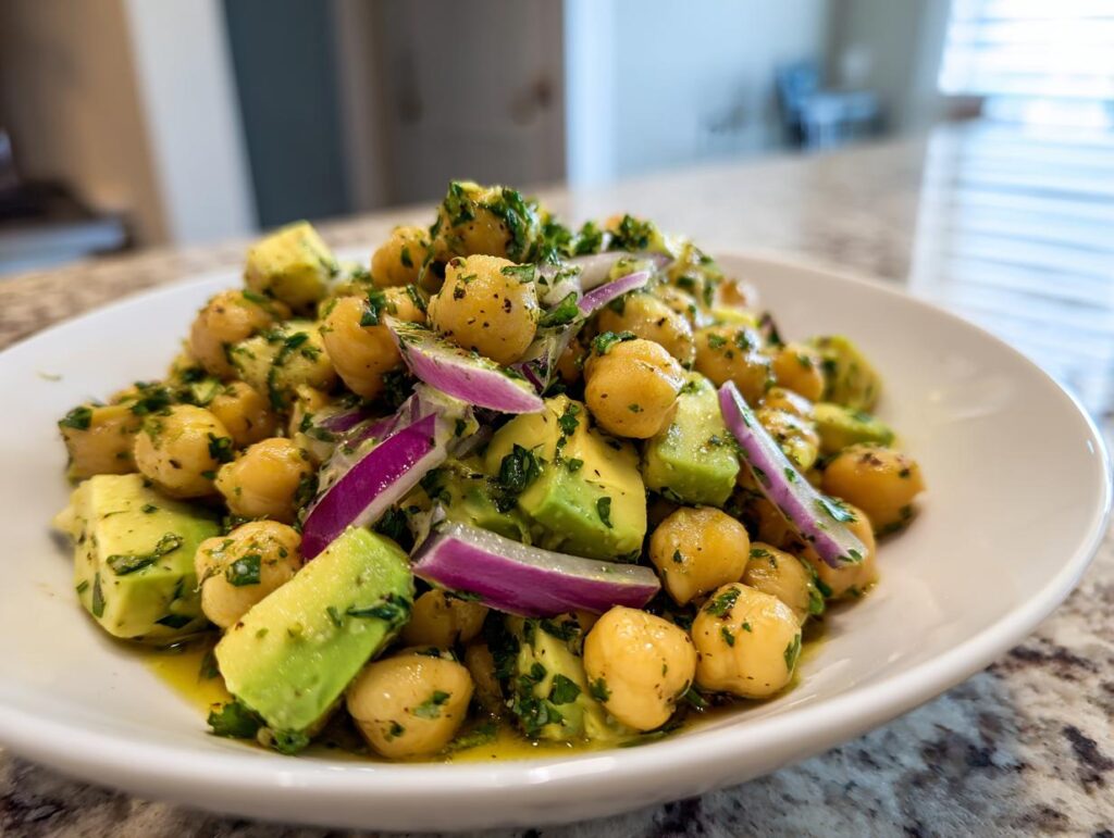Primer plano de una ensalada de garbanzos y aguacate con cebolla morada y perejil picado, ideal para cenas rápidas y baratas.
