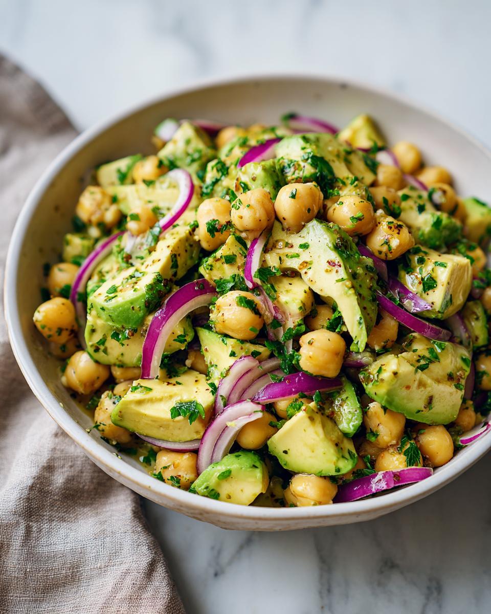 Primer plano de una ensalada de garbanzos y aguacate con cebolla roja y perejil, ideal para cenas rápidas y baratas.