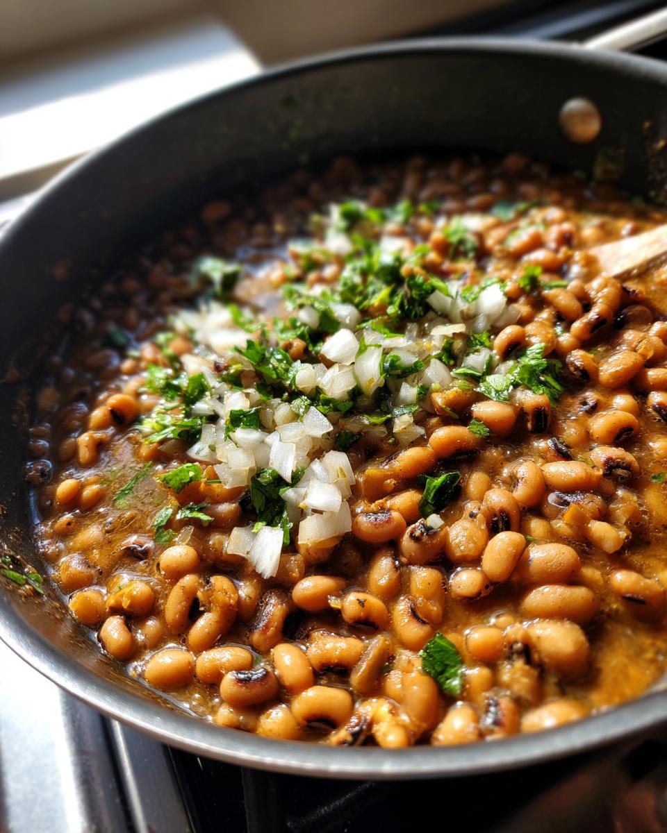 Primer plano de frijoles caritas cocinándose en una sartén con cebolla picada y cilantro fresco.