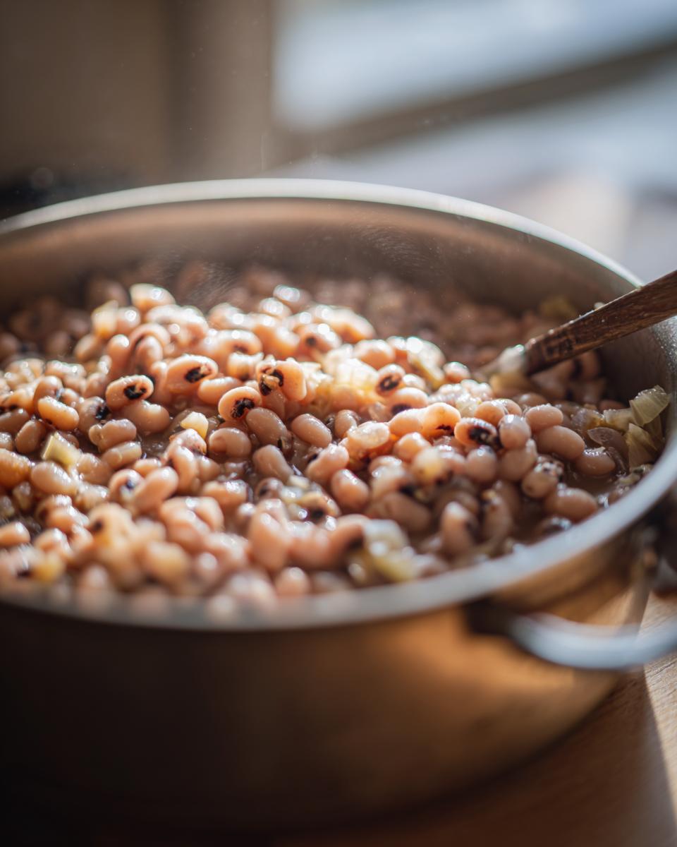 Primer plano de frijoles caritas cocinándose en una sartén con una cuchara de madera.