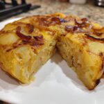 Primer plano de una jugosa tortilla de patatas, un corte revela las capas de patata y huevo, ideal para recetas virales TikTok España 2025.
