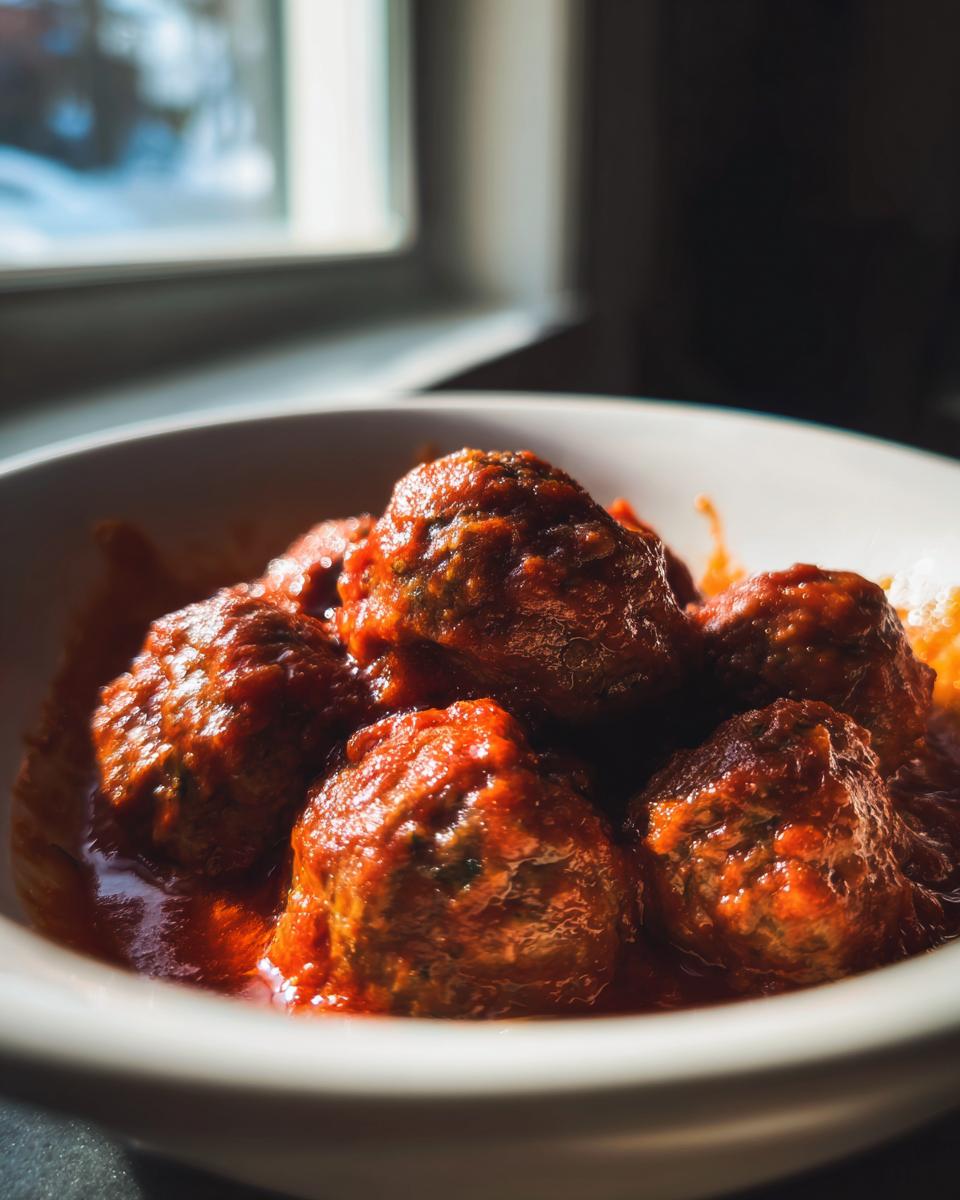Albóndigas caseras en salsa roja servidas en un plato blanco cerca de una ventana