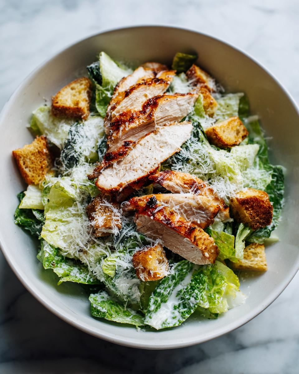 Ensalada César con pollo a la parrilla, lechuga, crutones y queso rallado como ideas de cenas ligeras.