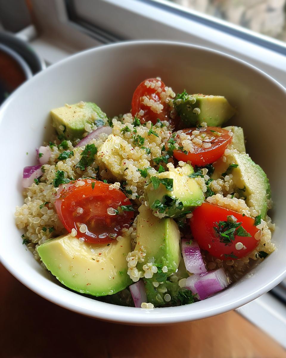 Ensalada con quinoa, aguacate, tomates cherry y cebolla morada en un bol blanco.