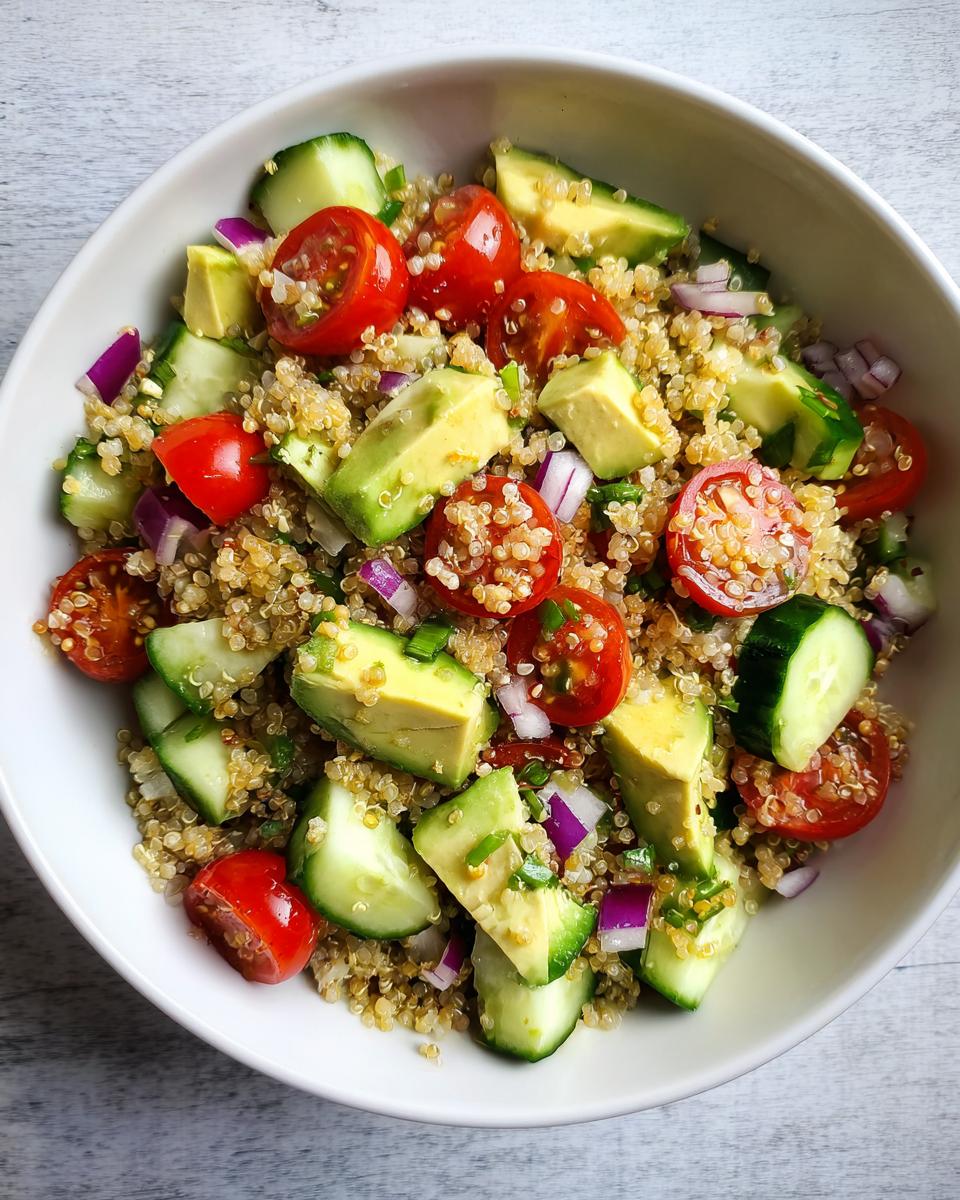 Ensalada de quinoa con aguacate, jitomates cherry, pepino y cebolla morada en un tazón blanco