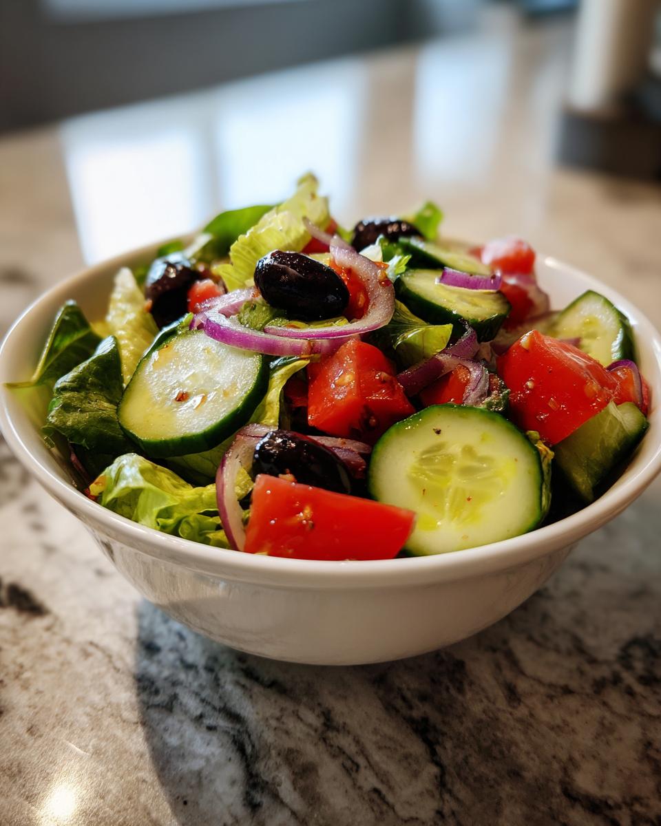 Ensalada saludable y fácil con lechuga, pepino, tomate, aceitunas negras y cebolla morada en un tazón blanco.