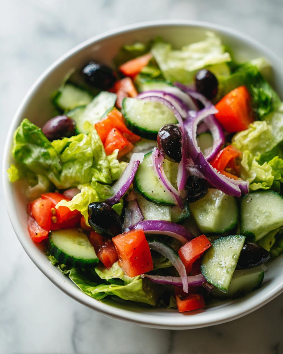 Ensalada saludable y fácil con lechuga, tomate, pepino, cebolla morada y aceitunas negras en bowl blanco