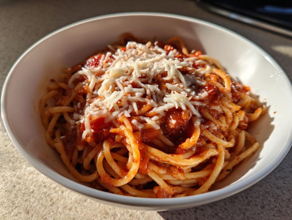 Plato blanco con espagueti con salsa roja y queso rallado, ideal para recetas para compartir en familia