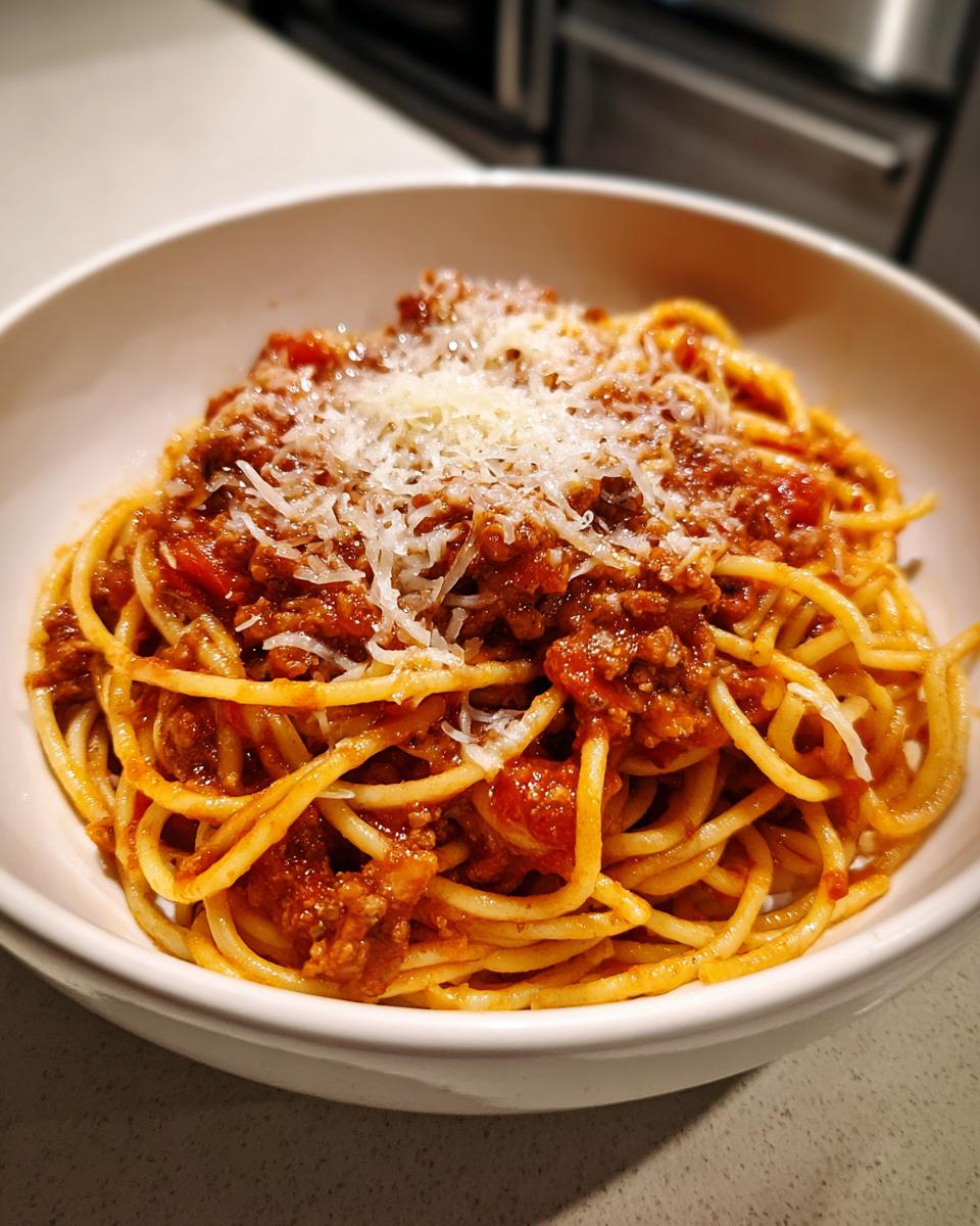 Plato blanco con espaguetis cubiertos de salsa boloñesa y queso rallado en la cima