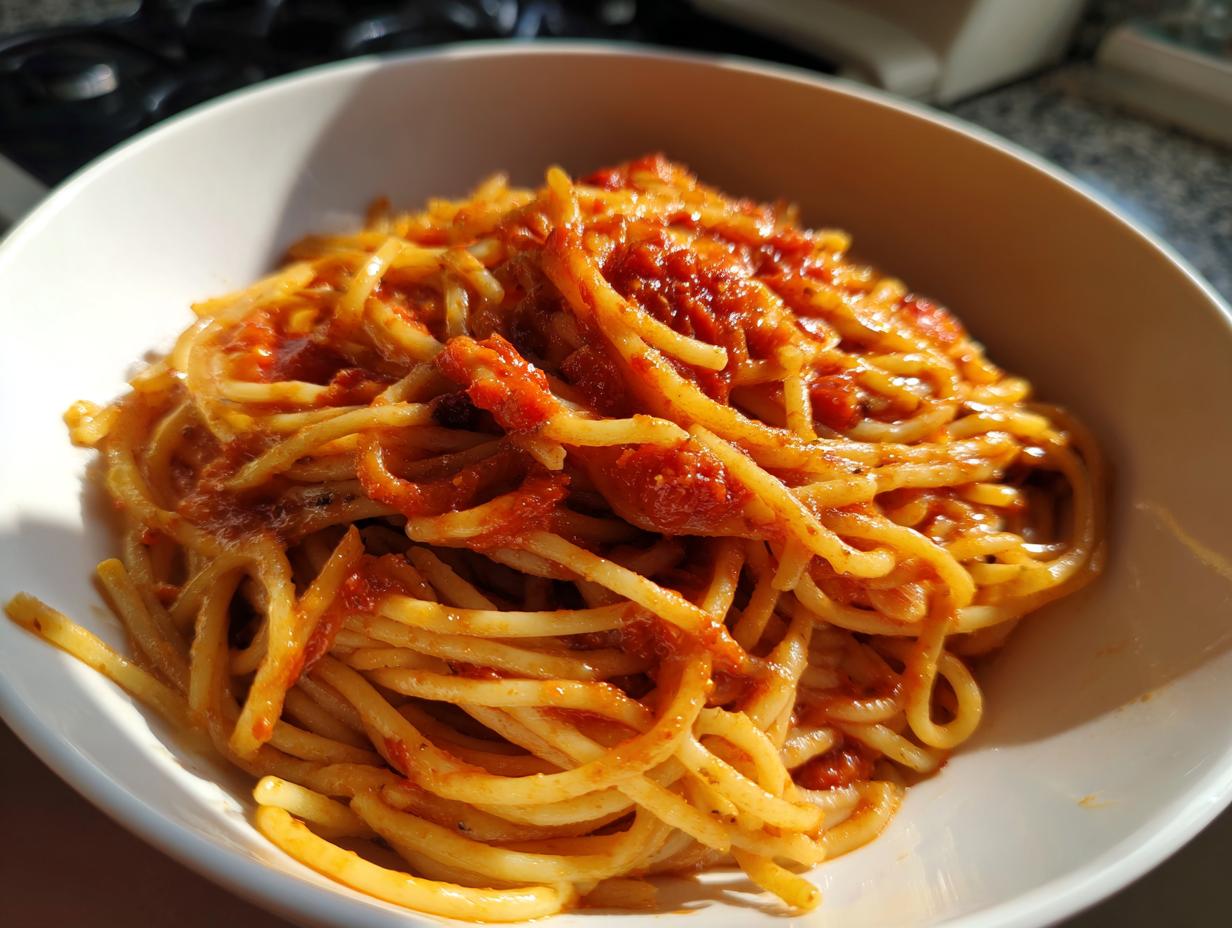 Plato blanco con espaguetis cubiertos de salsa de tomate, ideal para recetas económicas San Valentín.