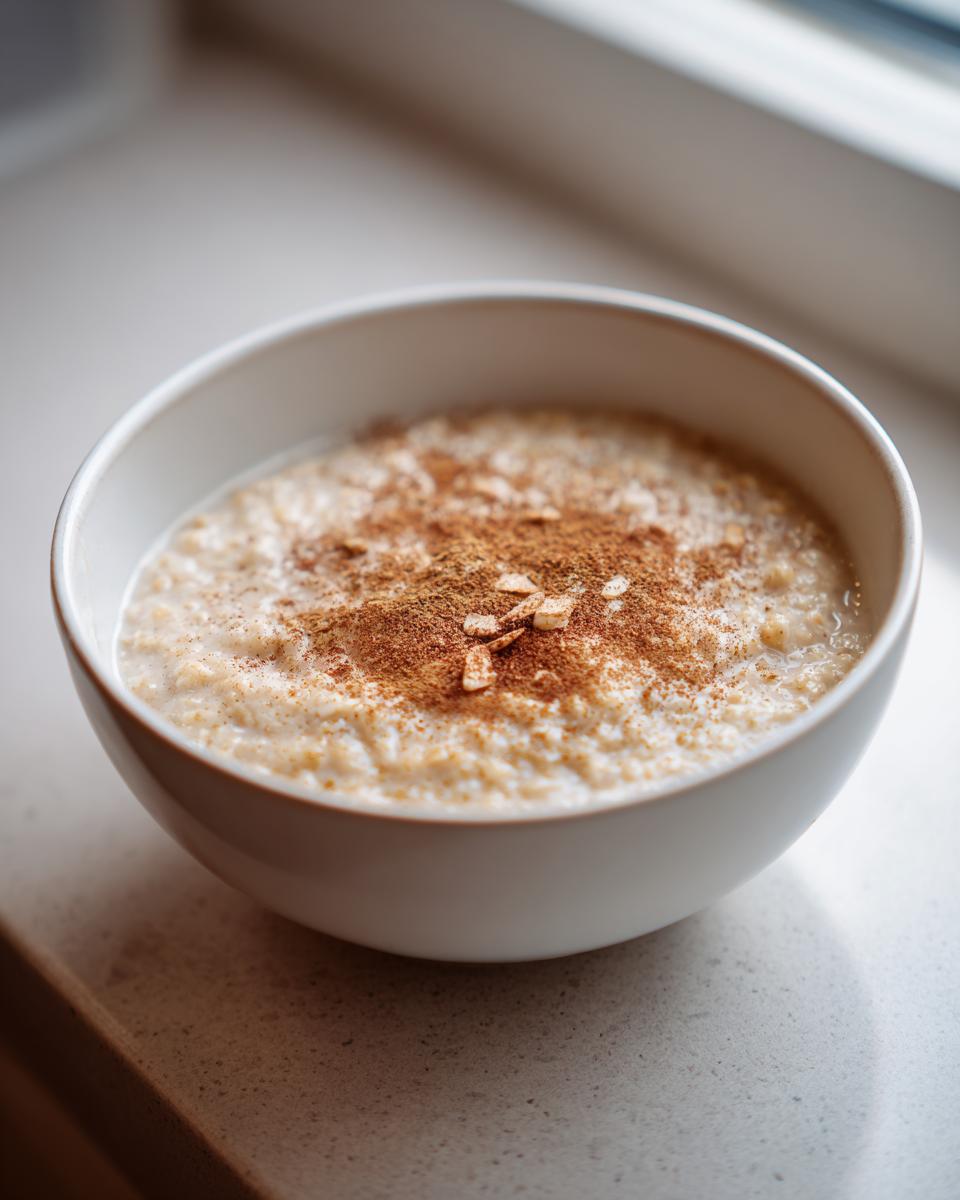 Tazón blanco con gachas de avena cremosas con canela espolvoreada encima.