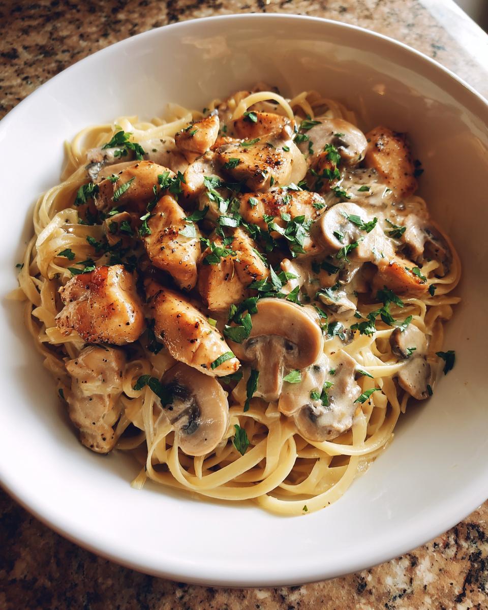 Plato de pasta con pollo y champiñones en salsa cremosa, decorado con perejil fresco