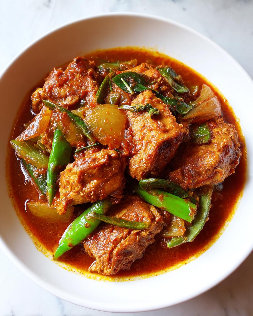 Plato de pollo guisado casero con trozos de pollo, pimientos verdes y cebolla en salsa roja