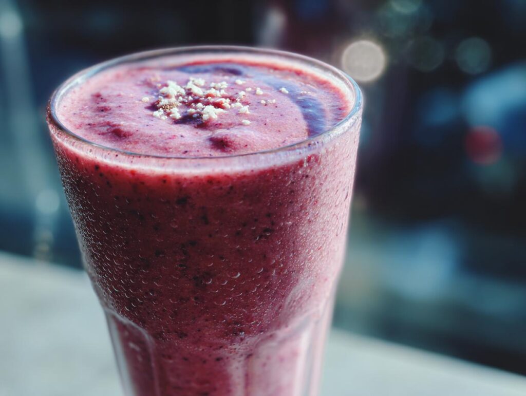 Smoothie rojo cremoso con textura espesa en un vaso con gotas de condensación.