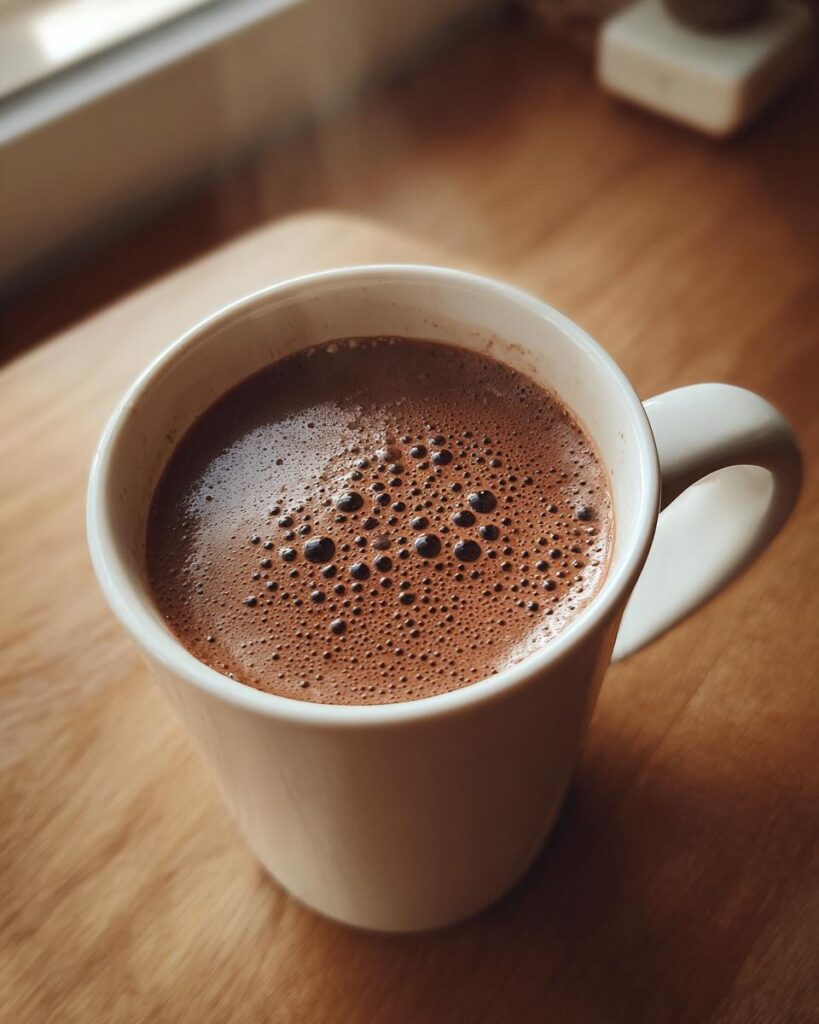 Primer plano de una taza blanca con chocolate caliente casero espumoso sobre mesa de madera