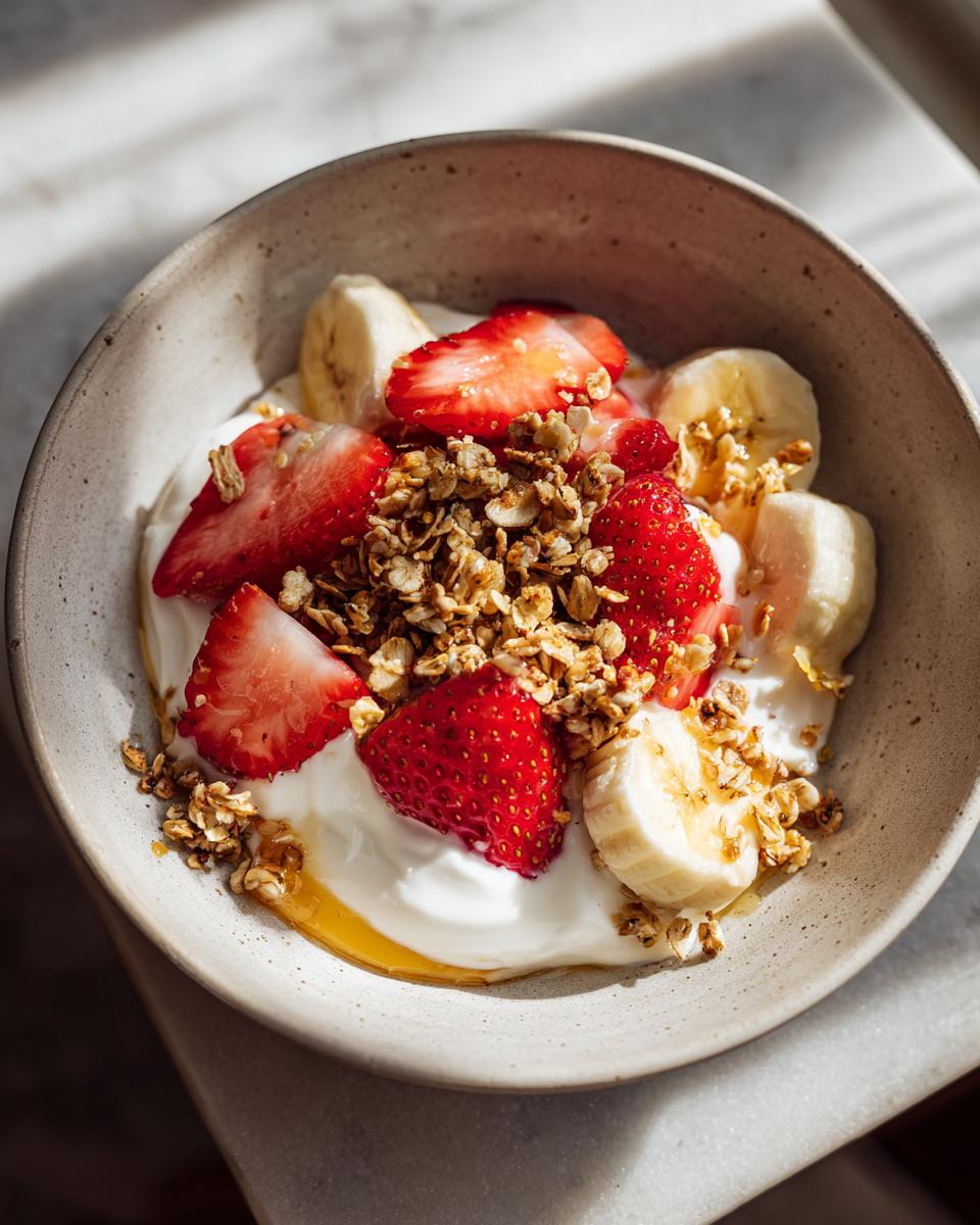 Tazón con yogur, fresas, rodajas de plátano y granola para recetas de merienda saludable
