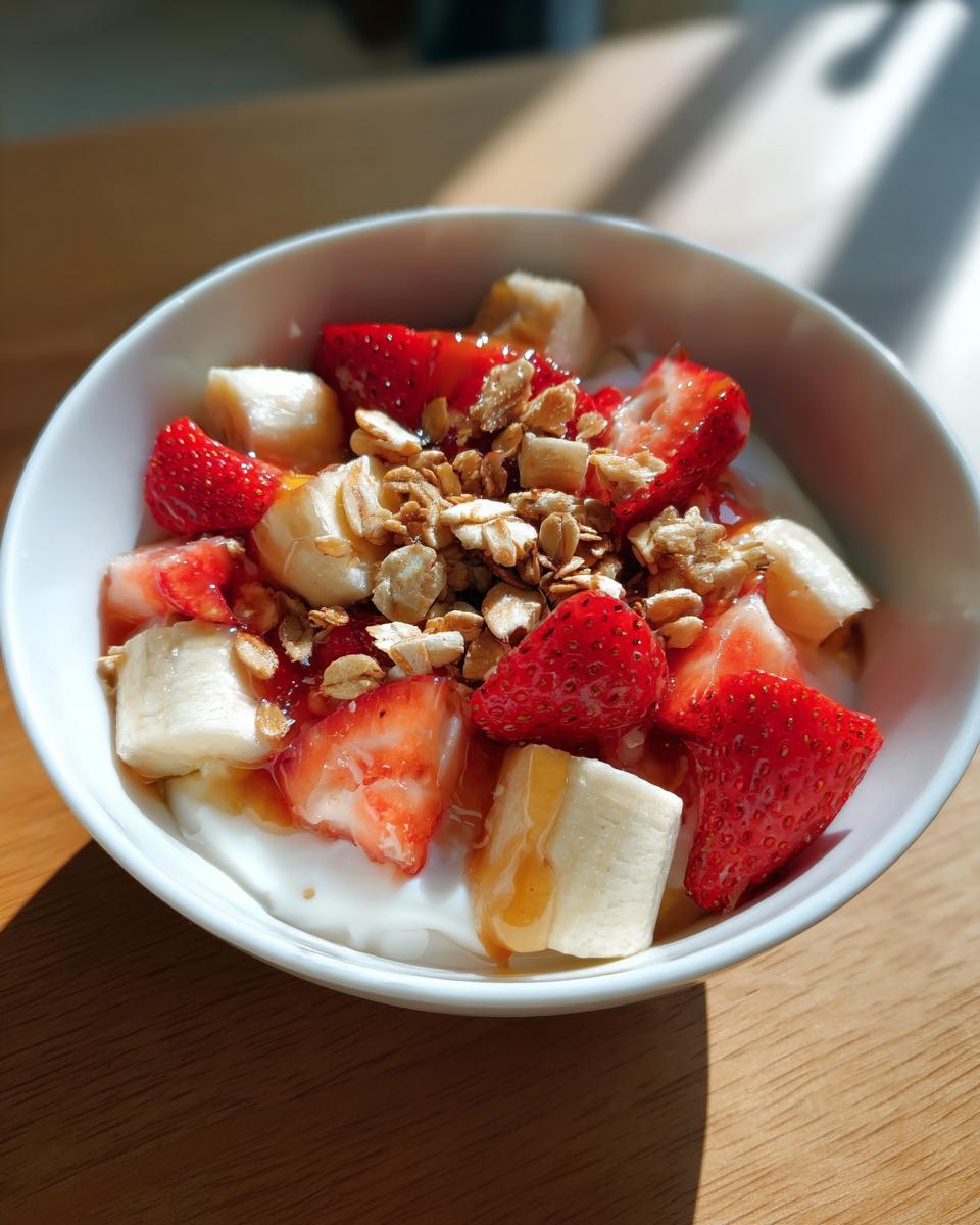 Tazón de yogur con fresas, plátano, granola y miel como recetas de merienda saludable.
