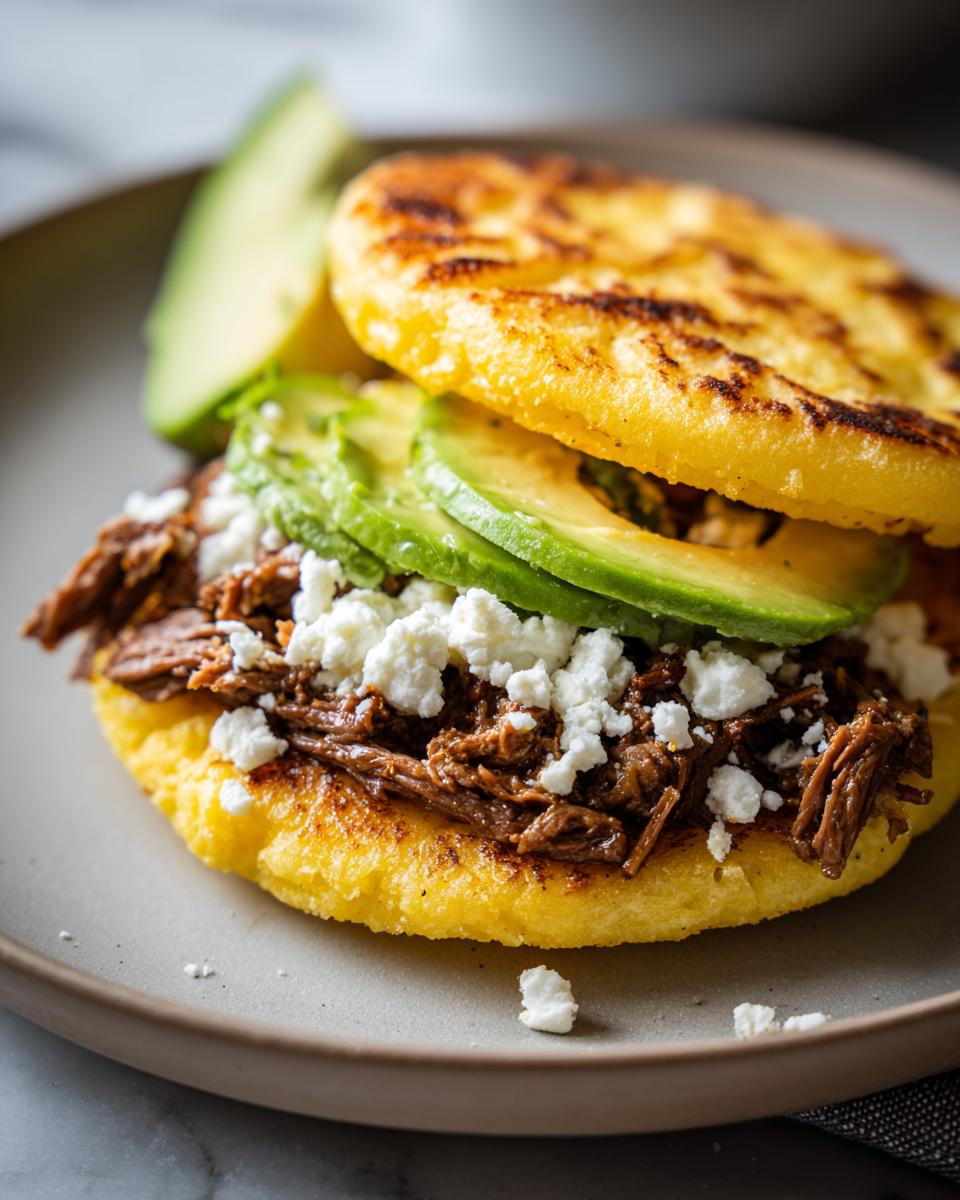 Arepa rellena fáciles con carne deshebrada, queso fresco y rodajas de aguacate en plato
