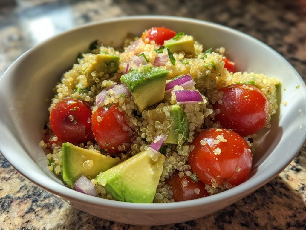 Ensalada con quinoa, aguacate, tomate cherry y cebolla morada en un bowl blanco.