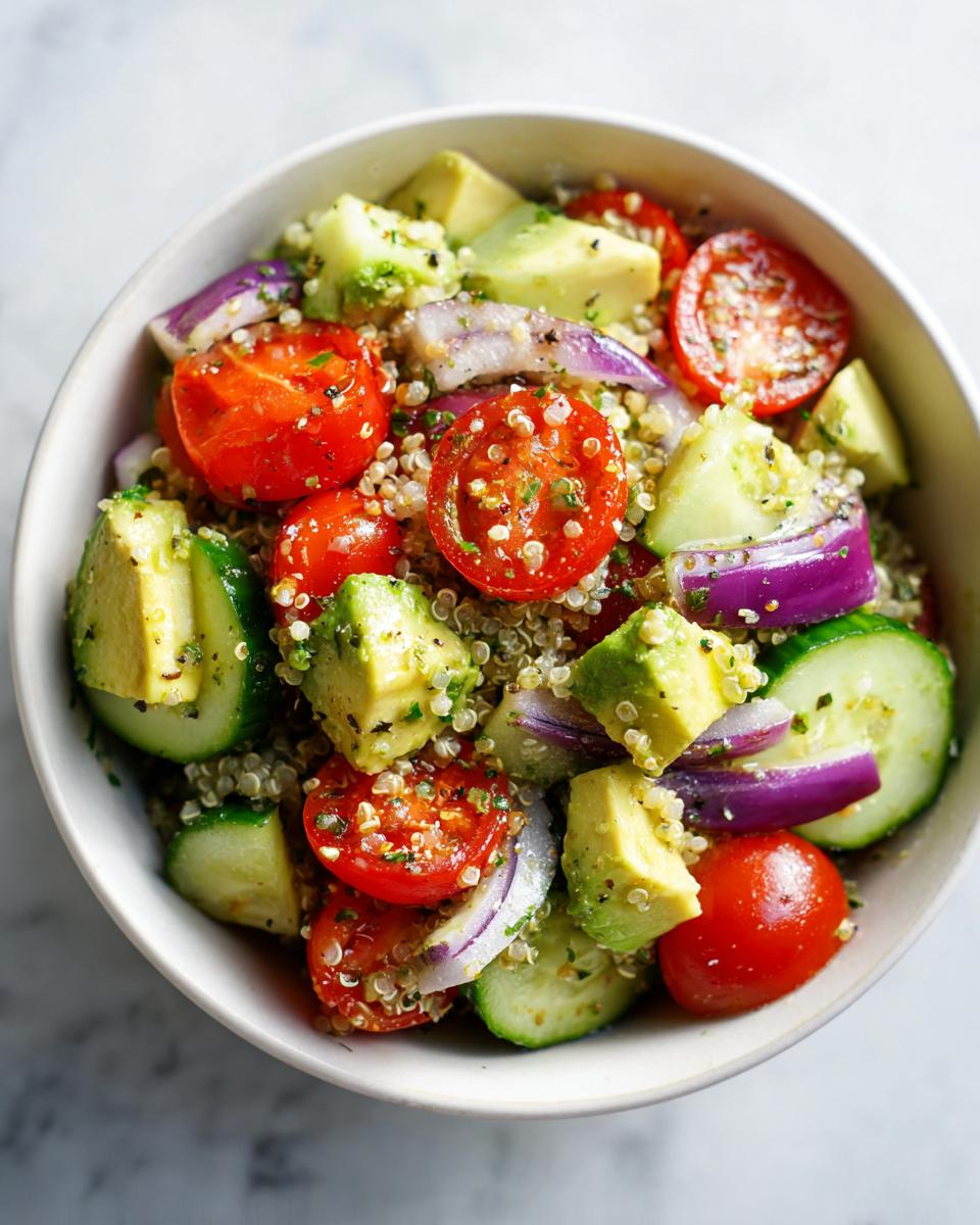 Ensalada fresca con quinoa, tomate cherry, aguacate, pepino y cebolla morada en un bol blanco.