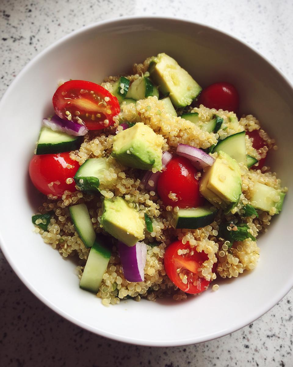 Bowl blanco con ensalada de quinoa, aguacate, tomate cherry, pepino y cebolla morada