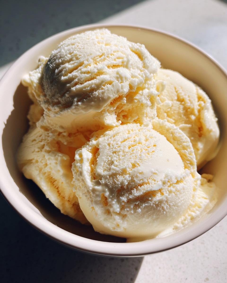 Tres bolas de helado casero de vainilla servidas en un bol blanco bajo luz natural.