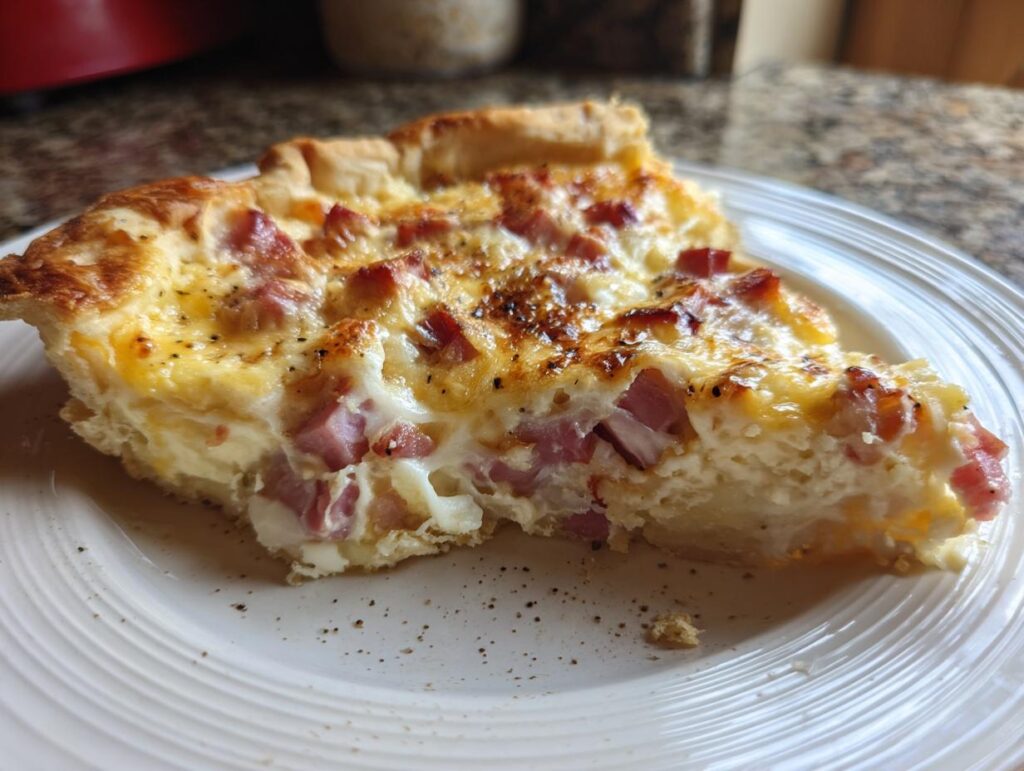 Porción de quiche casero con jamón y queso en un plato blanco, receta al horno faciles