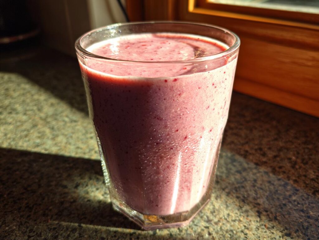 Vaso con smoothie saludable de frutas color rosa sobre mesa cerca de ventana
