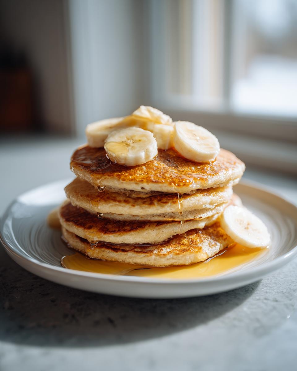 Tortitas de avena saludables apiladas con rodajas de plátano y miel en plato blanco