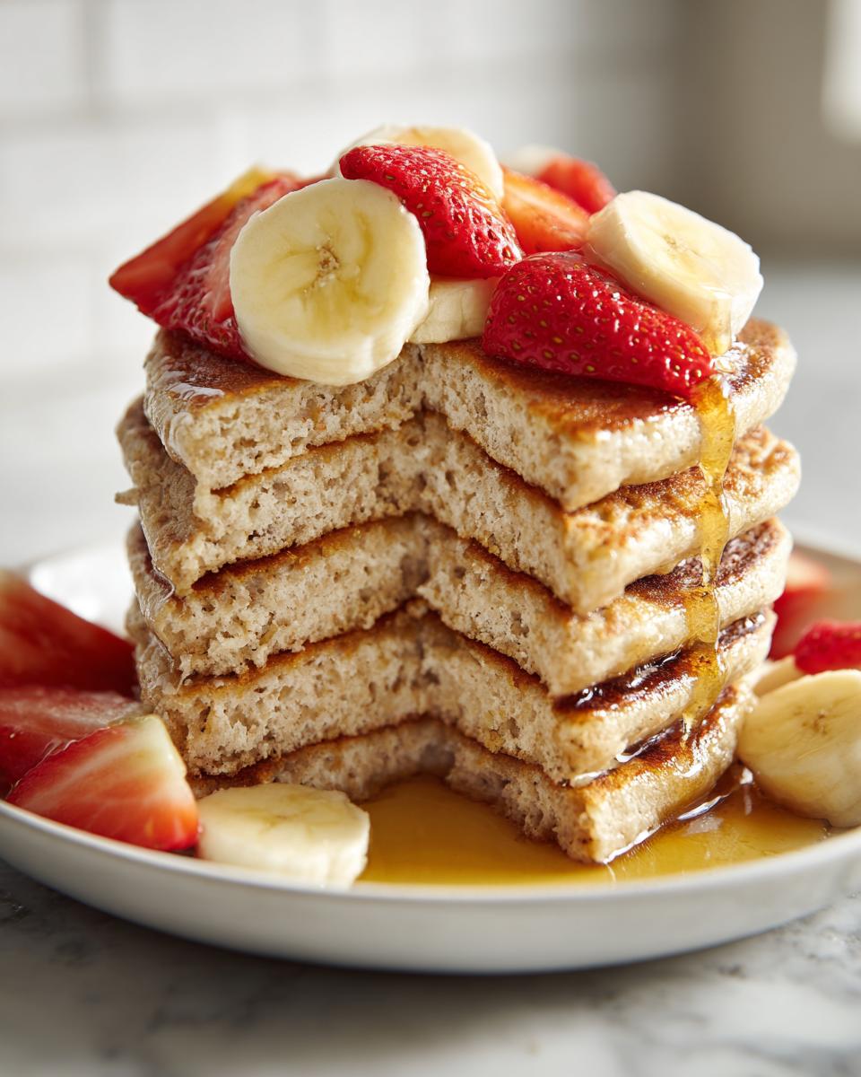 Tortitas proteicas apiladas con rodajas de plátano, fresas y miel derramándose