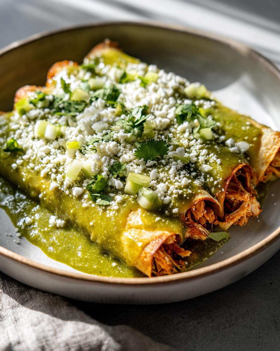 Plato de enchiladas verdes caseras rellenas de pollo, cubiertas con salsa verde, queso fresco y cilantro.