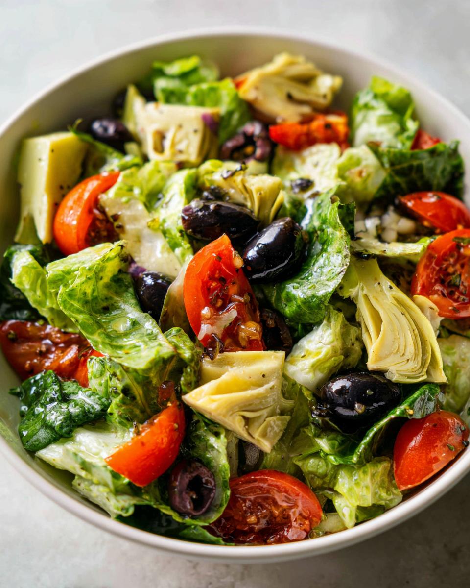 Ensalada con alcachofas, aceitunas negras, tomates cherry y lechuga fresca en un bol blanco