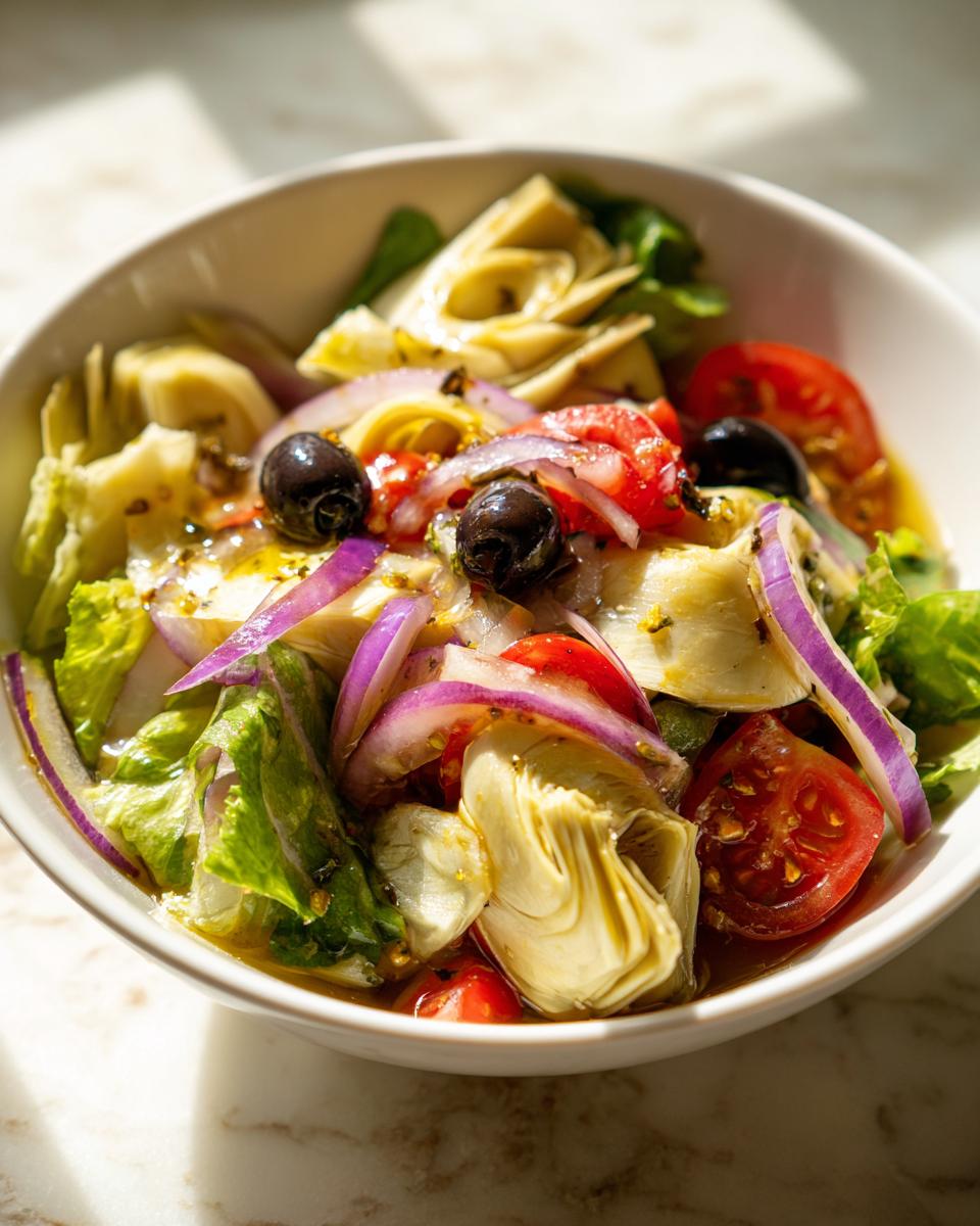 Ensalada con alcachofas, tomate, cebolla morada, aceitunas negras y lechuga en un bol blanco
