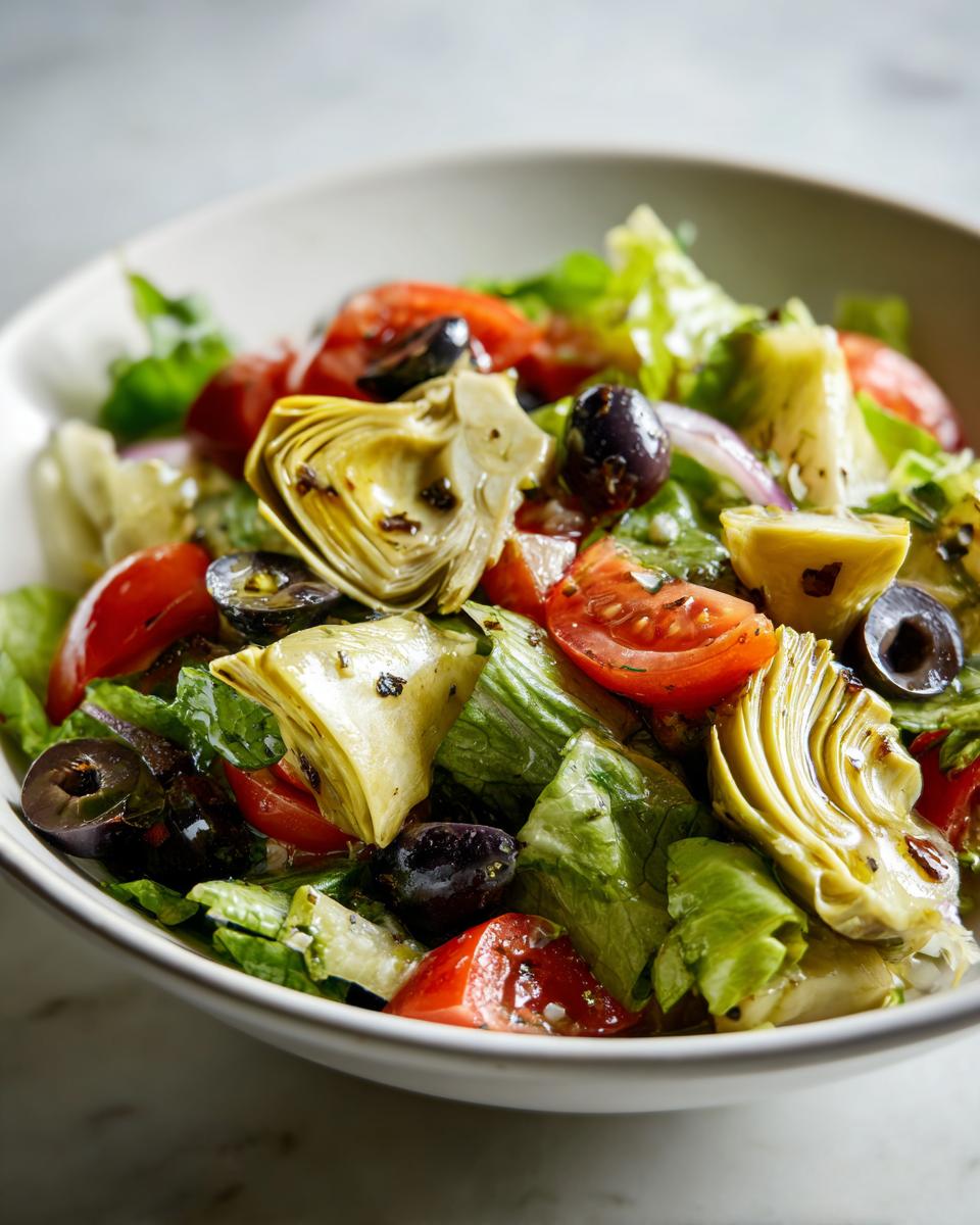 Ensalada con alcachofas, tomates cherry, aceitunas negras y lechuga fresca en un plato blanco.