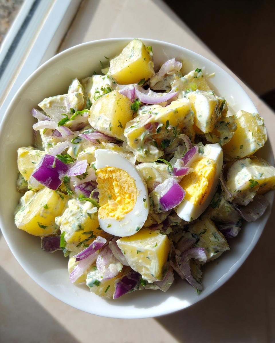 Ensalada de papa con huevo y cebolla morada en un tazón blanco, ideal para recetas para el 1 de mayo