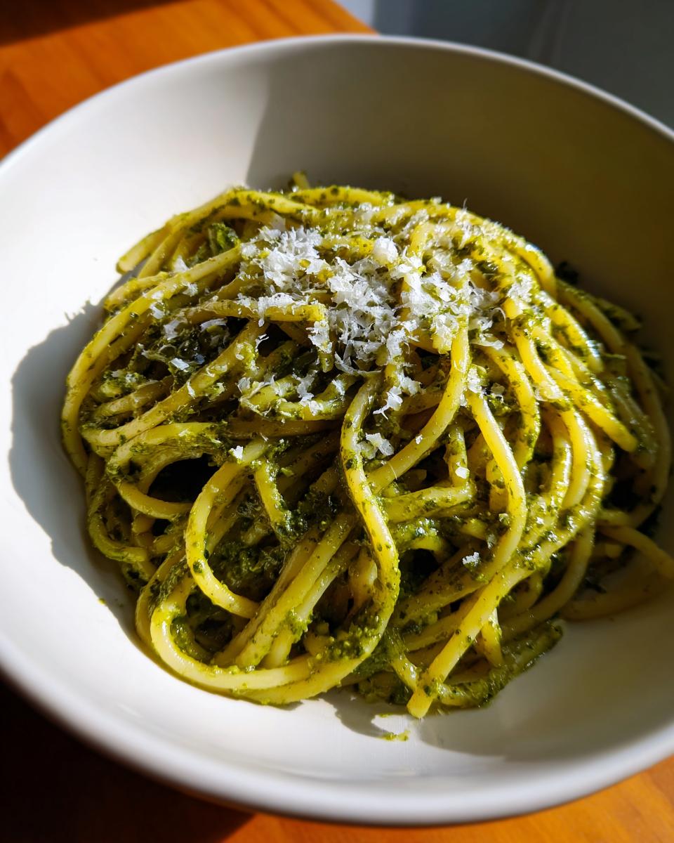 Tazón blanco con pasta al pesto cubierta con queso rallado.