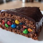 Rebanada de tarta piñata de chocolate sorpresa con cobertura brillante y caramelos de colores en el interior.