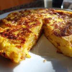 Tortilla española clásica con un trozo cortado mostrando su interior jugoso y dorado