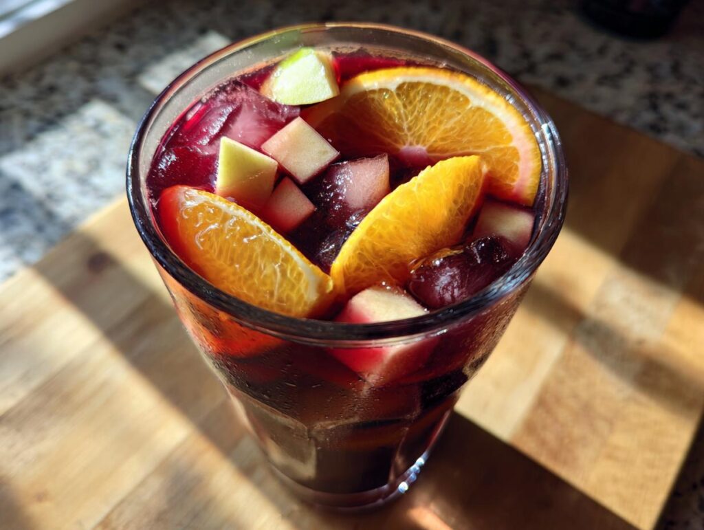 Vaso de sangría sin alcohol con rodajas de naranja, cubos de manzana y hielo.